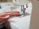 Seamstress at work. Seamstress's left hand makes a seam on a soft fabric using a sewing machine close-up
