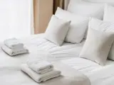 Cropped view of white bedclothes and towels on bed in comfortable hotel room, hypoallergenic pillows, personal comfort idea, bedding concept, bathroom details